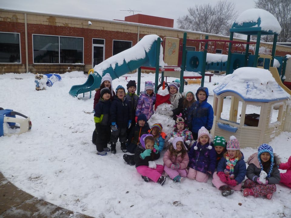 Group of children in winter clothing on a snowy playground with a snowman