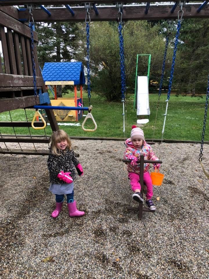 Two children on a playground, one standing and one on a swing