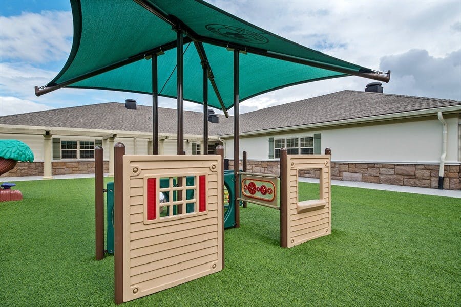 Playground structure with a green shade canopy over artificial turf