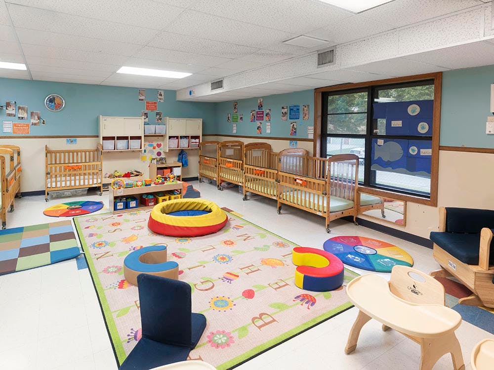 Cribs, play mats, and low chairs in a nursery or daycare room