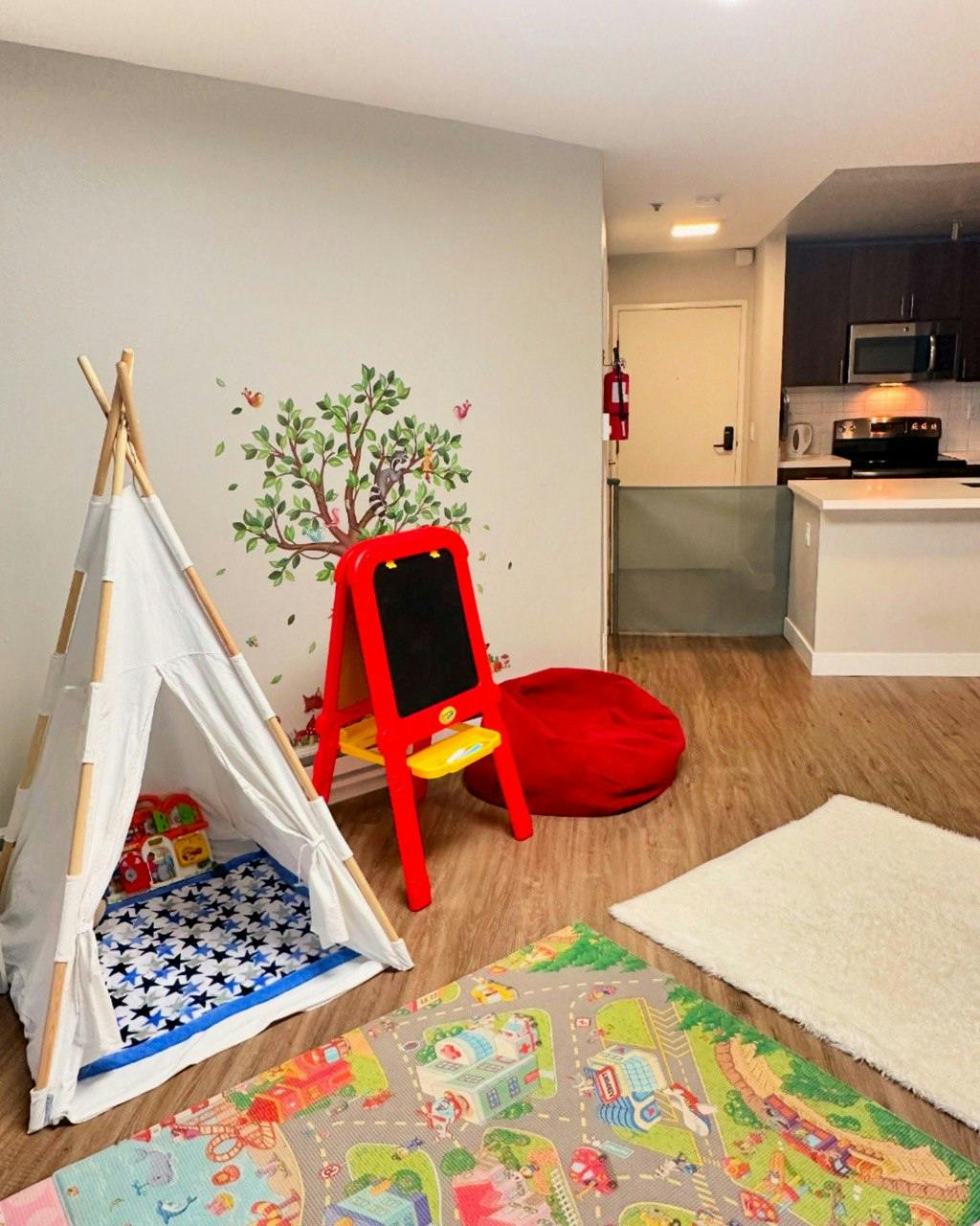 Play area with a white teepee, red easel, and colorful rugs on a wooden floor