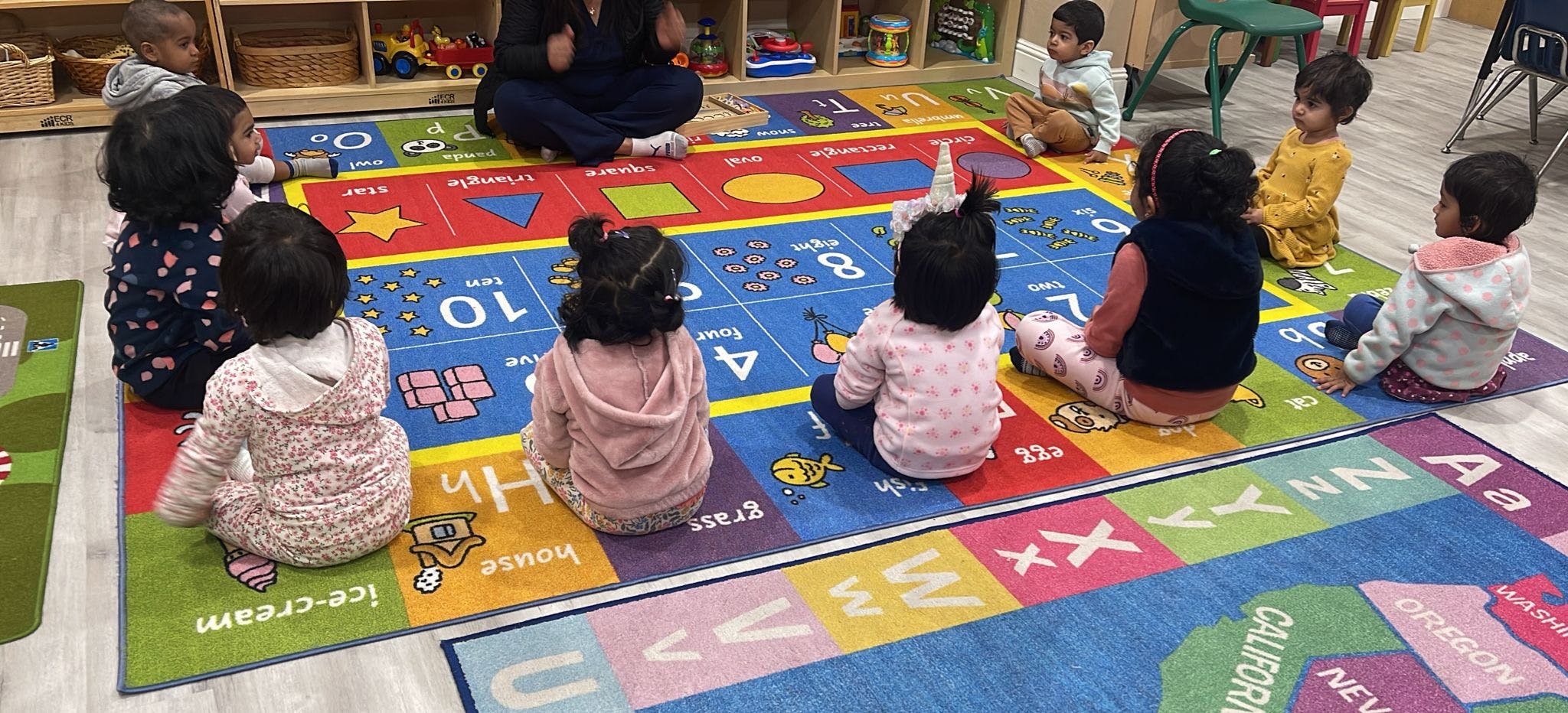 Children sitting on a colorful alphabet rug in a classroom