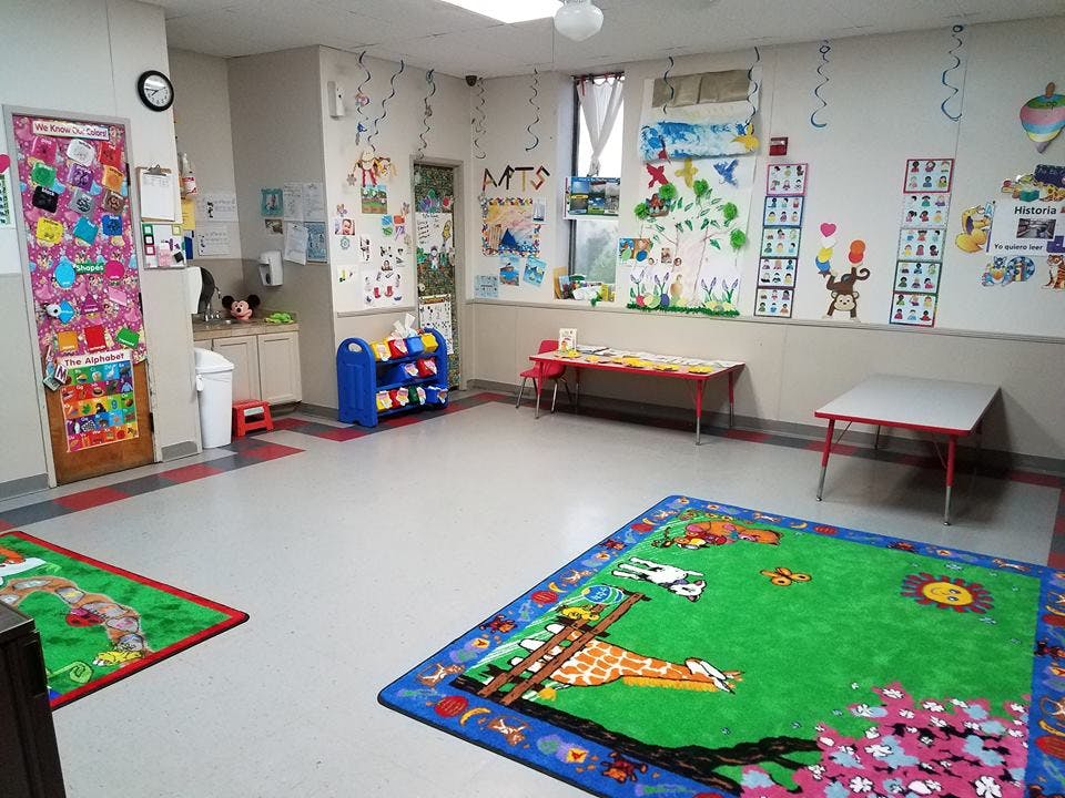 Empty classroom with colorful rugs and children's artwork on walls