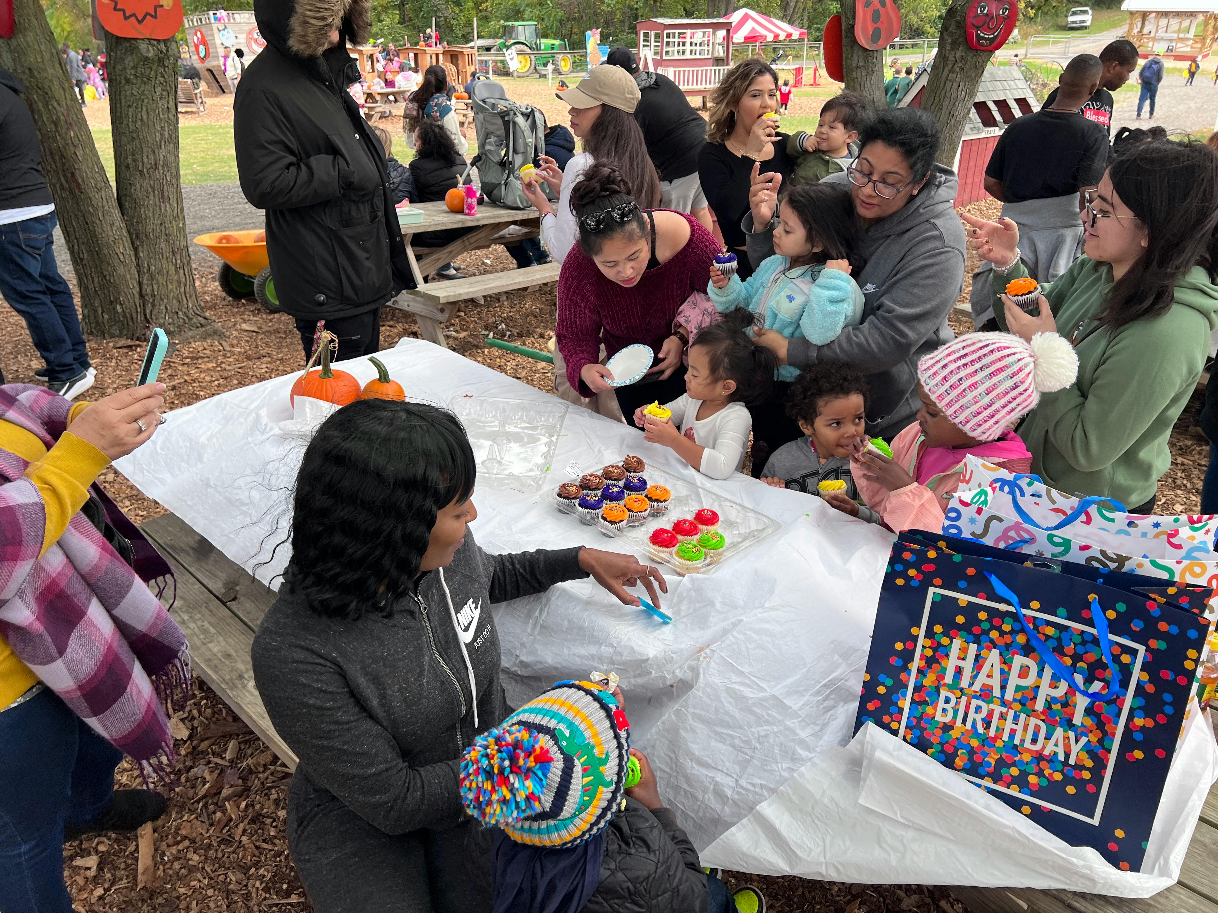 People and children gathered around a picnic table with cupcakes and a Happy Birthday bag