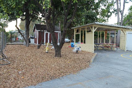 Outdoor area with wood chips, trees, a small shed, and a covered patio with picnic tables