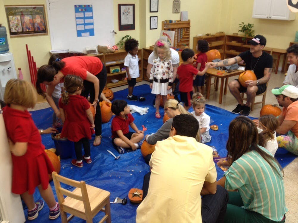 Adults and children carving pumpkins in a classroom