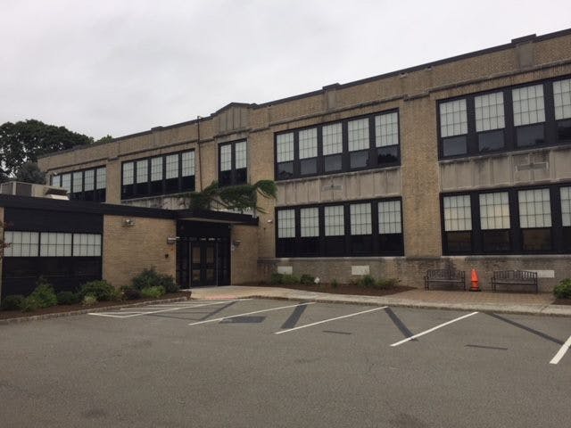 Exterior of a two-story building with many windows and a parking lot in front