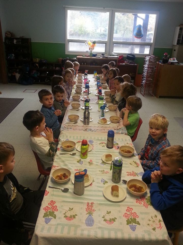 Children sitting at a long table with bowls and plates in a classroom