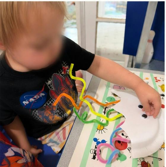 Child placing a googly eye on a paper plate craft with pipe cleaners