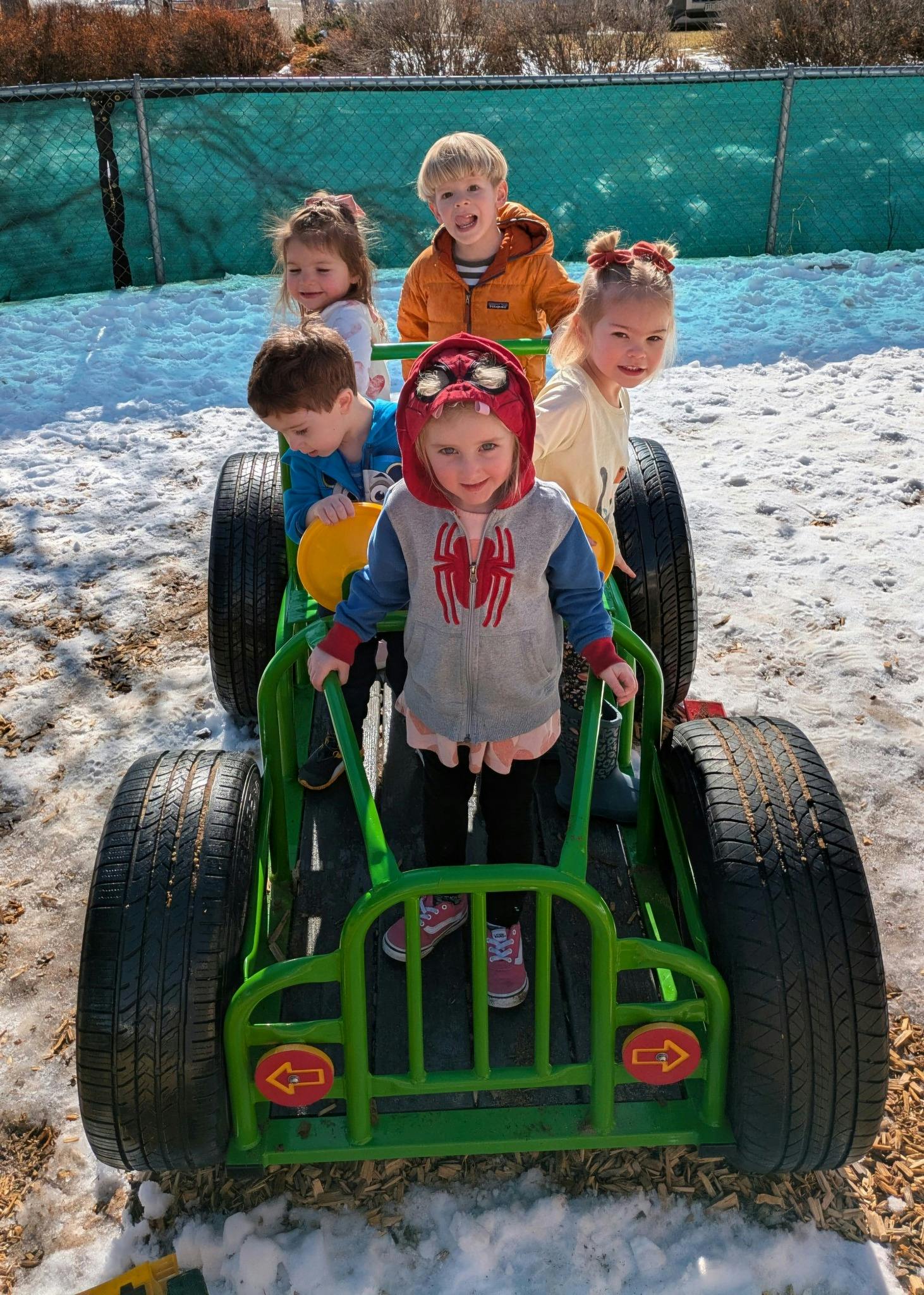 Five children playing in a green toy car in the snow