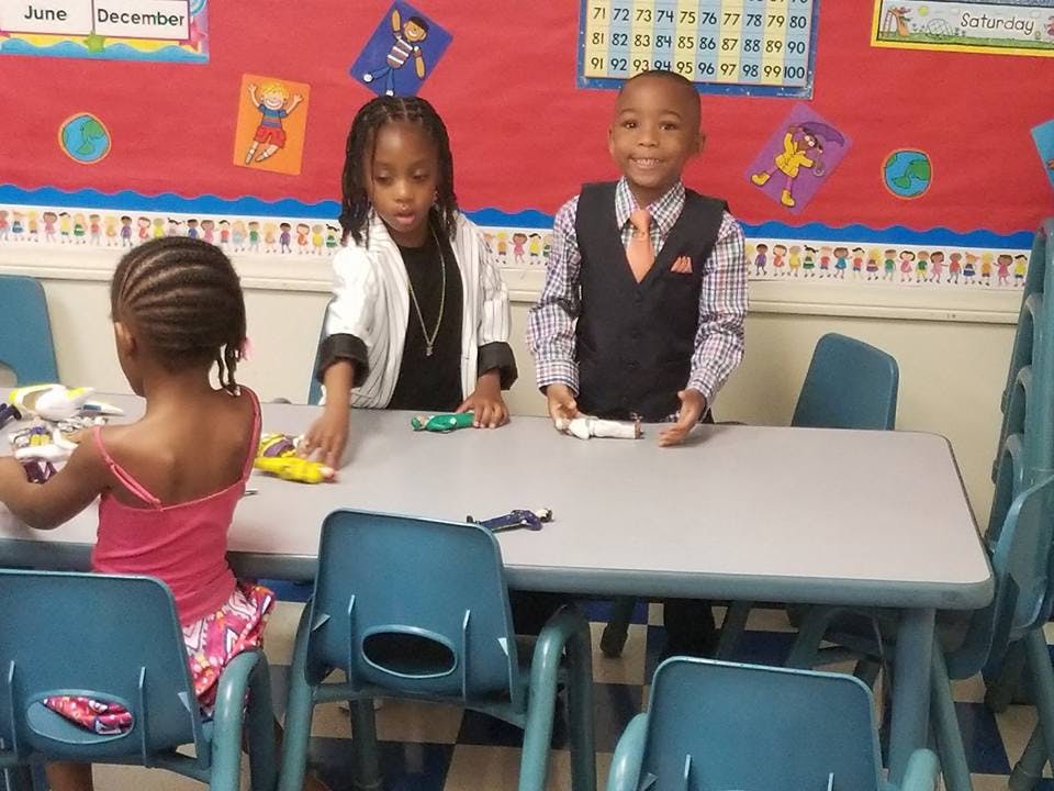 Three children standing and sitting at a table in a classroom
