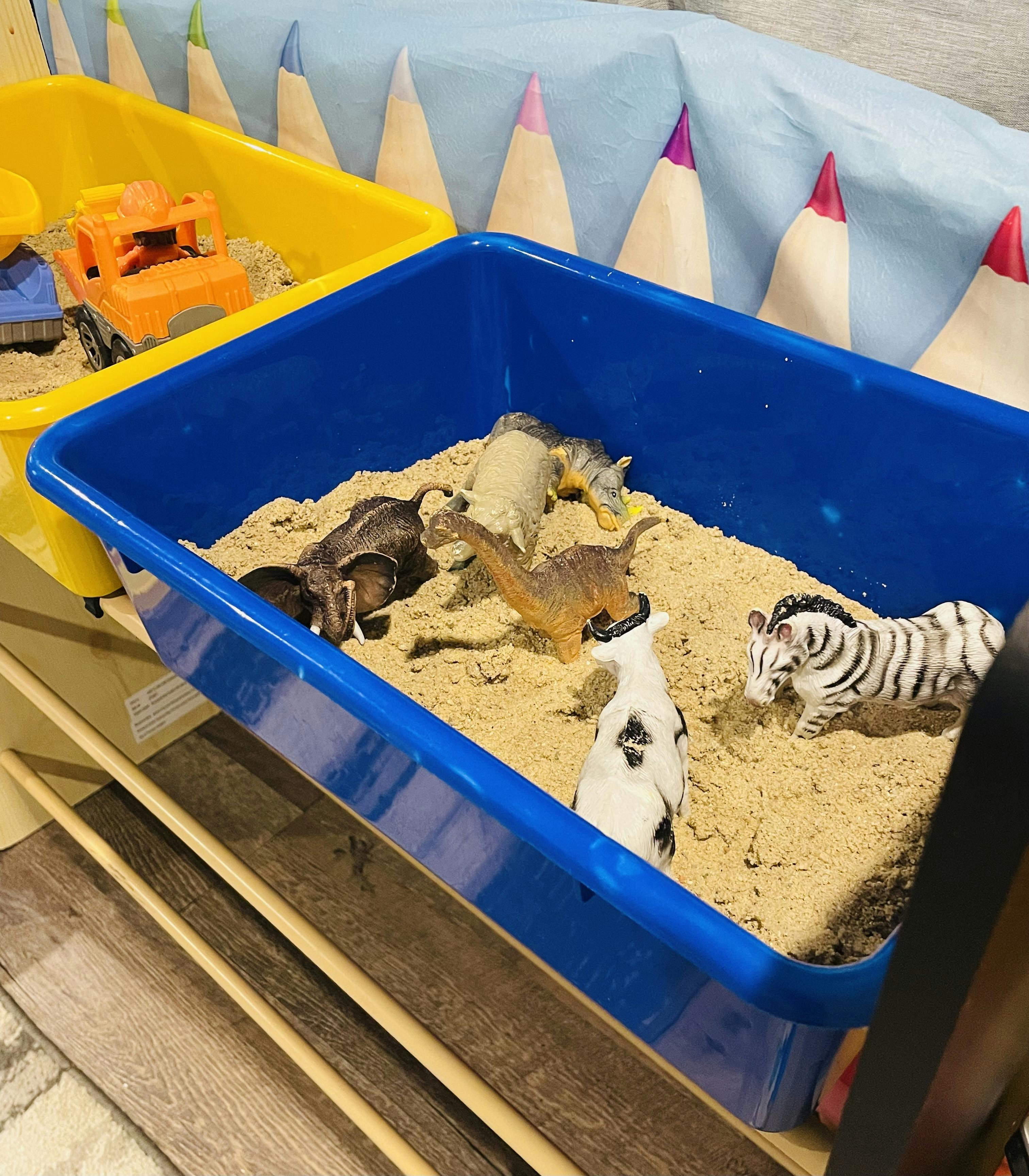 Plastic animal figurines in a blue bin filled with sensory sand