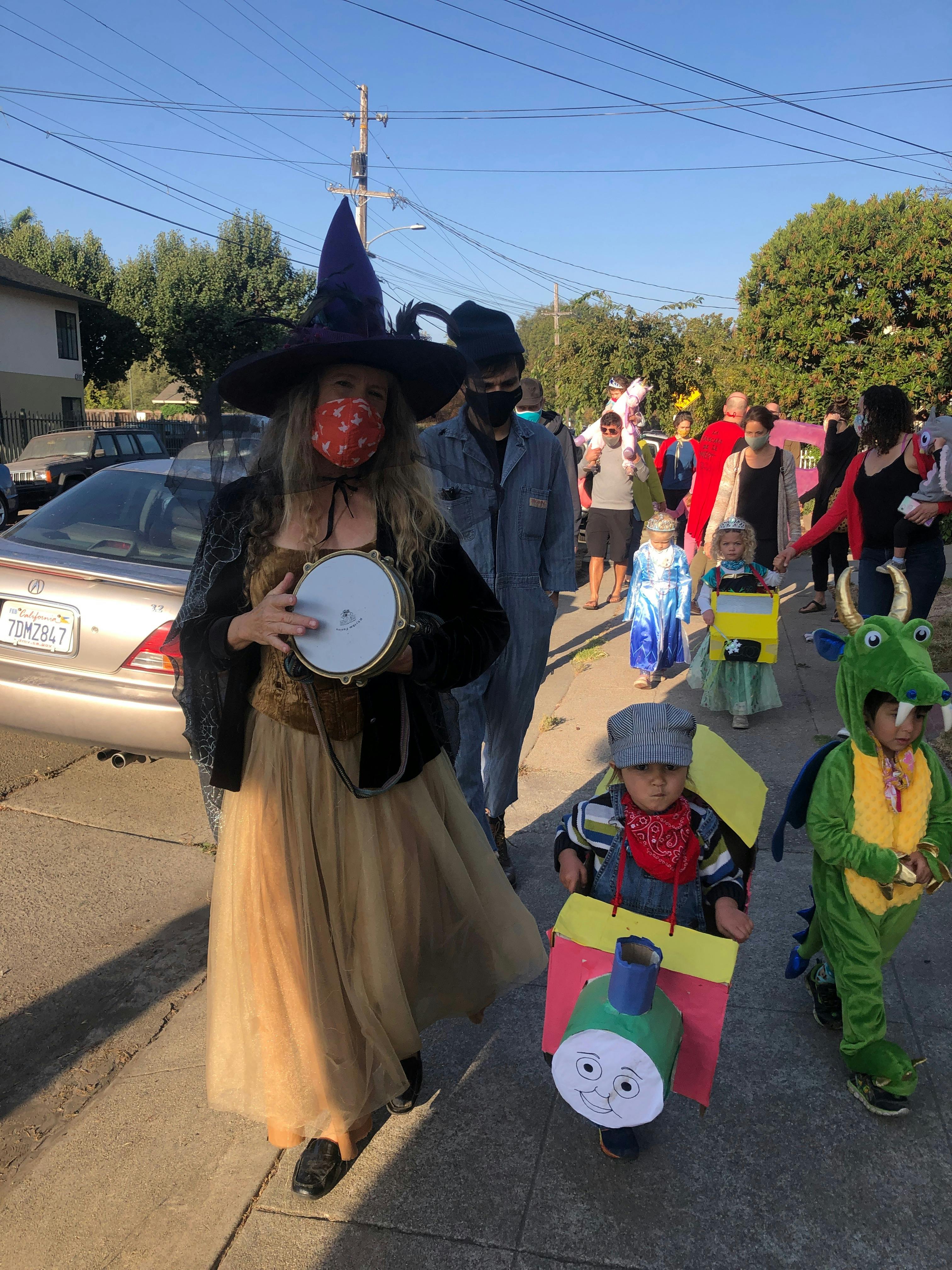 Person in witch costume holding a tambourine, children in costumes