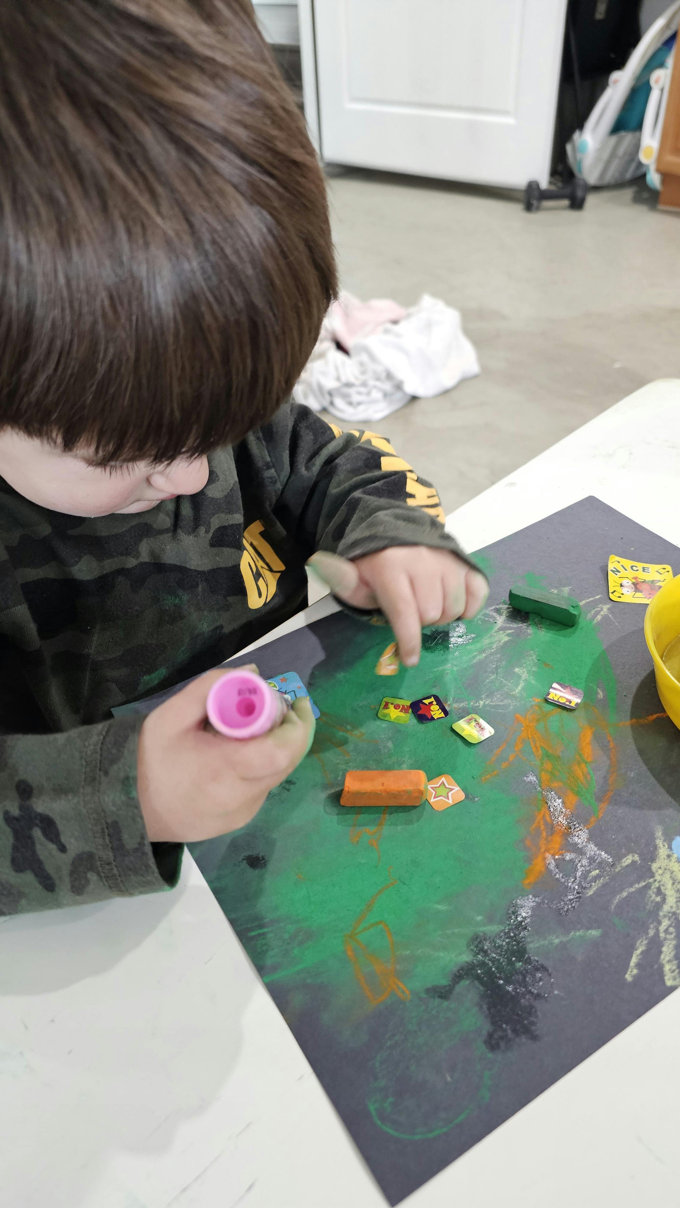 Child playing with stickers and glue stick on a dark paper