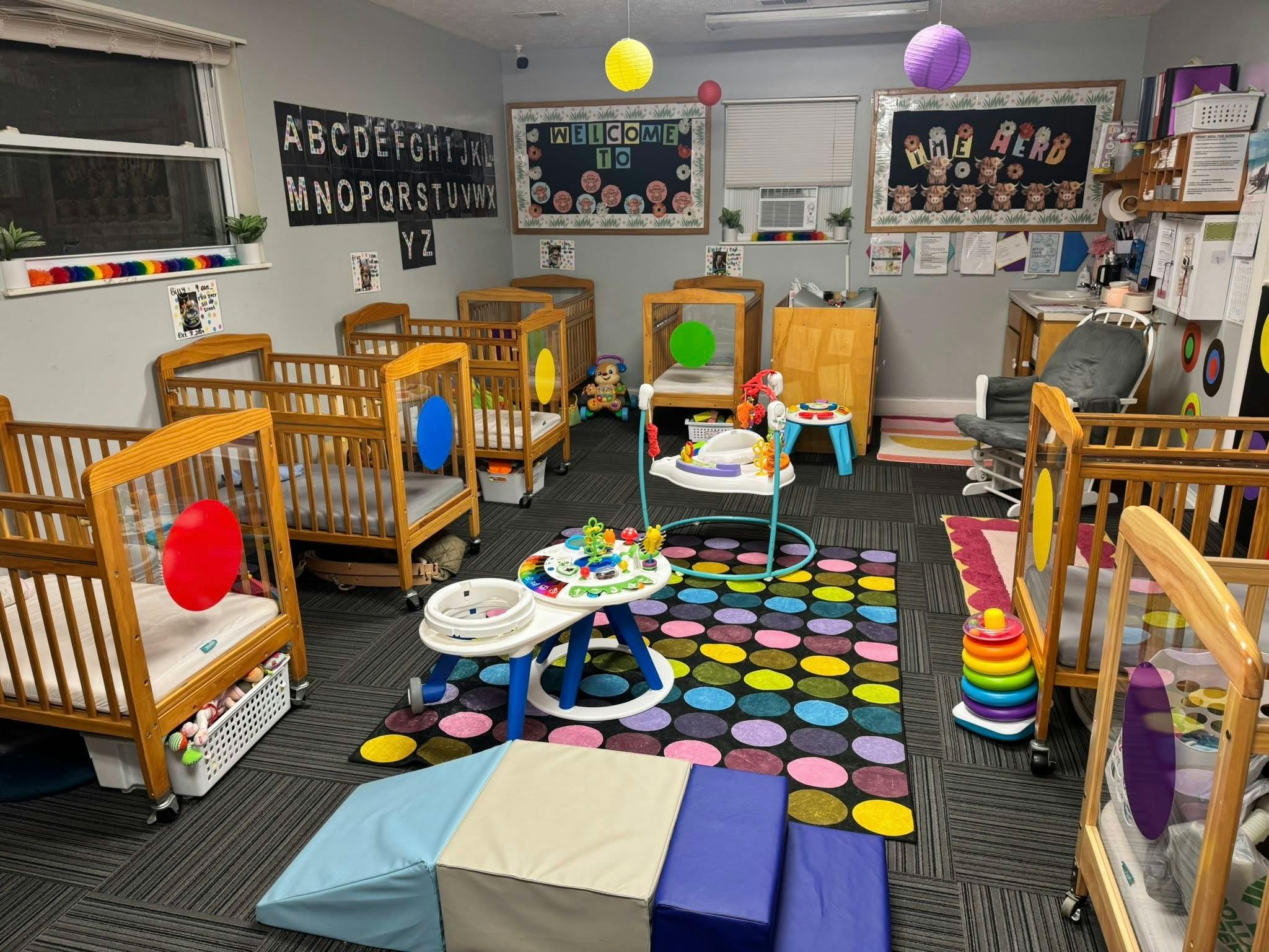 A classroom with multiple wooden cribs, play mats, and learning materials