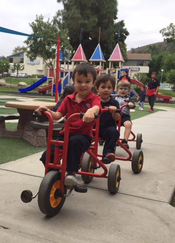 Three children riding red tricycles on a playground