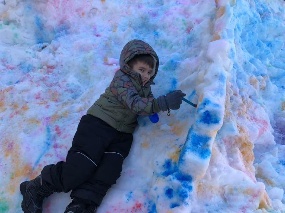 Child painting on snow with blue color