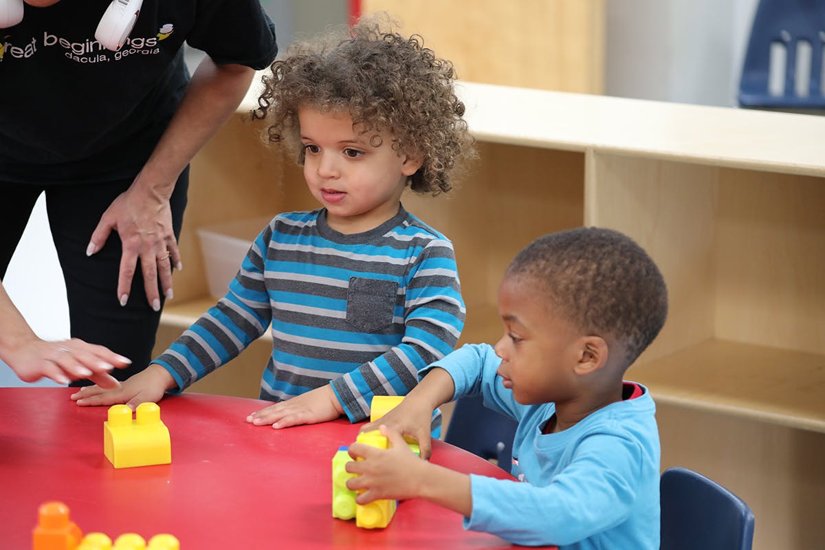 Two children playing with building blocks at a table in a classroom