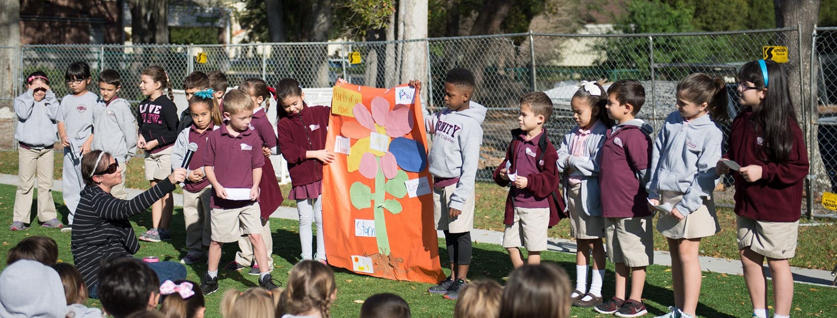 Adult and children gathered around a colorful banner outdoors