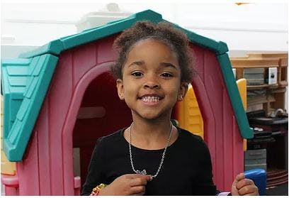 Child smiling in front of a playhouse