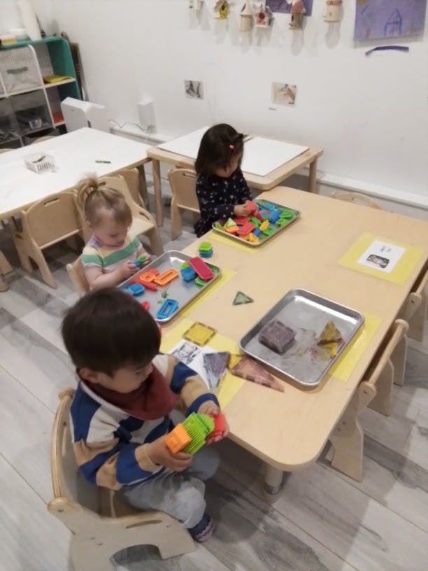 Three children playing with toys at small tables in a classroom