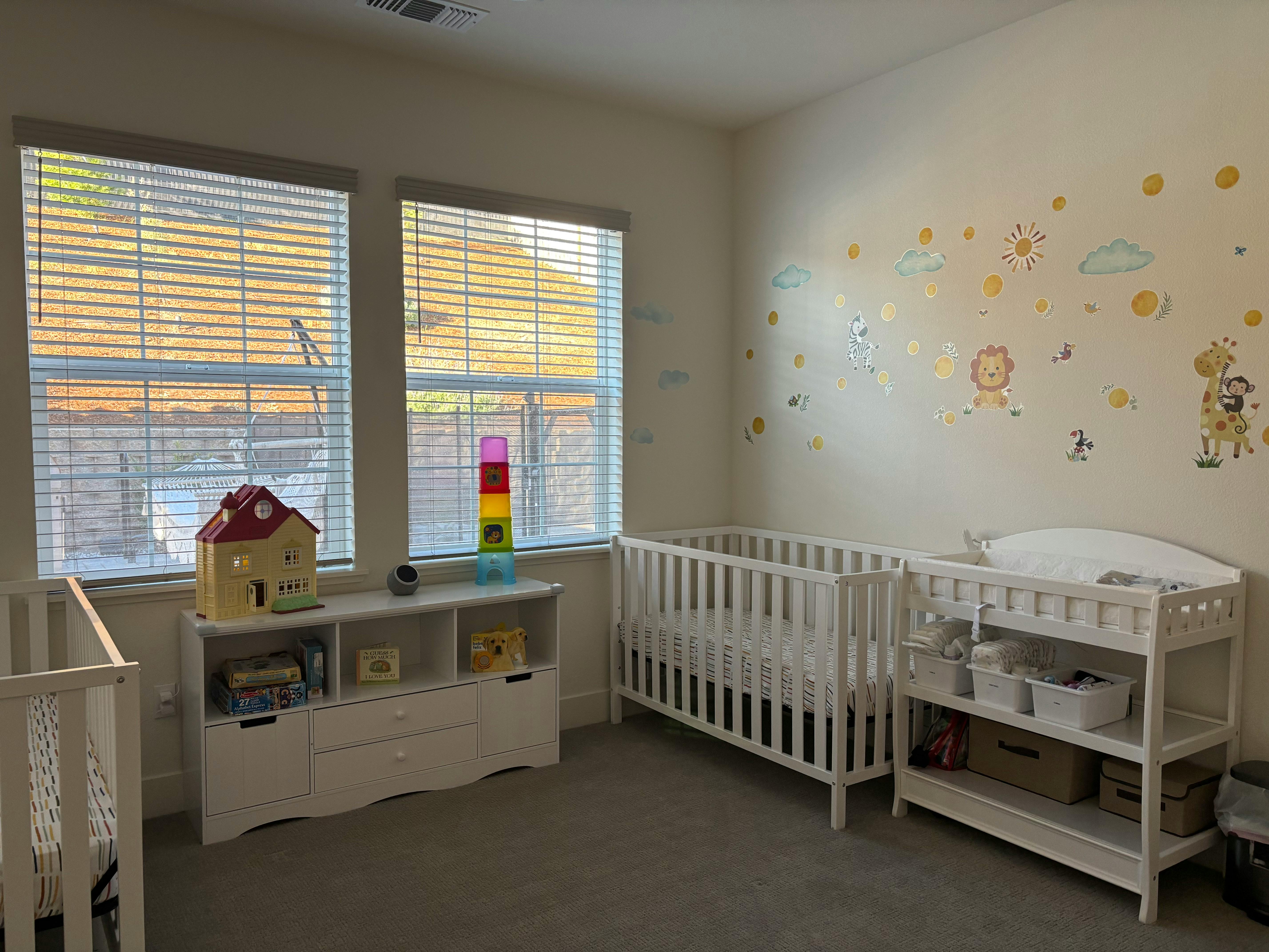 Nursery room with two cribs, a changing table, and a toy shelf