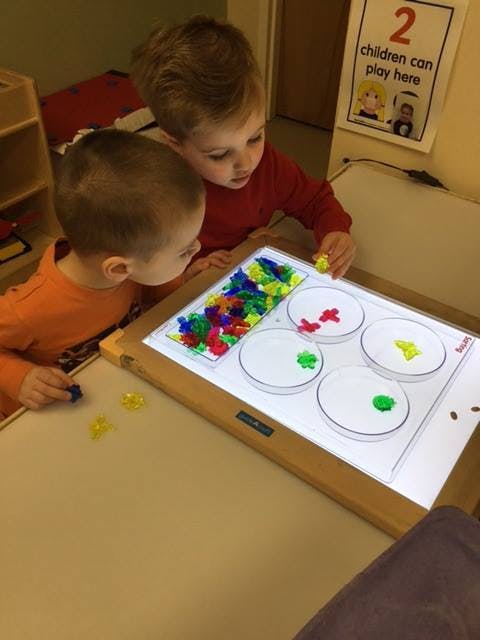 Two children playing with colorful manipulatives on a light table