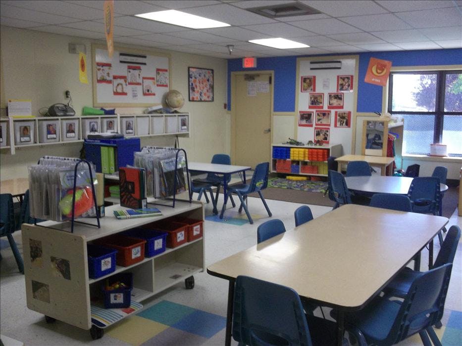 Empty classroom with tables, chairs, and shelves against blue and beige walls