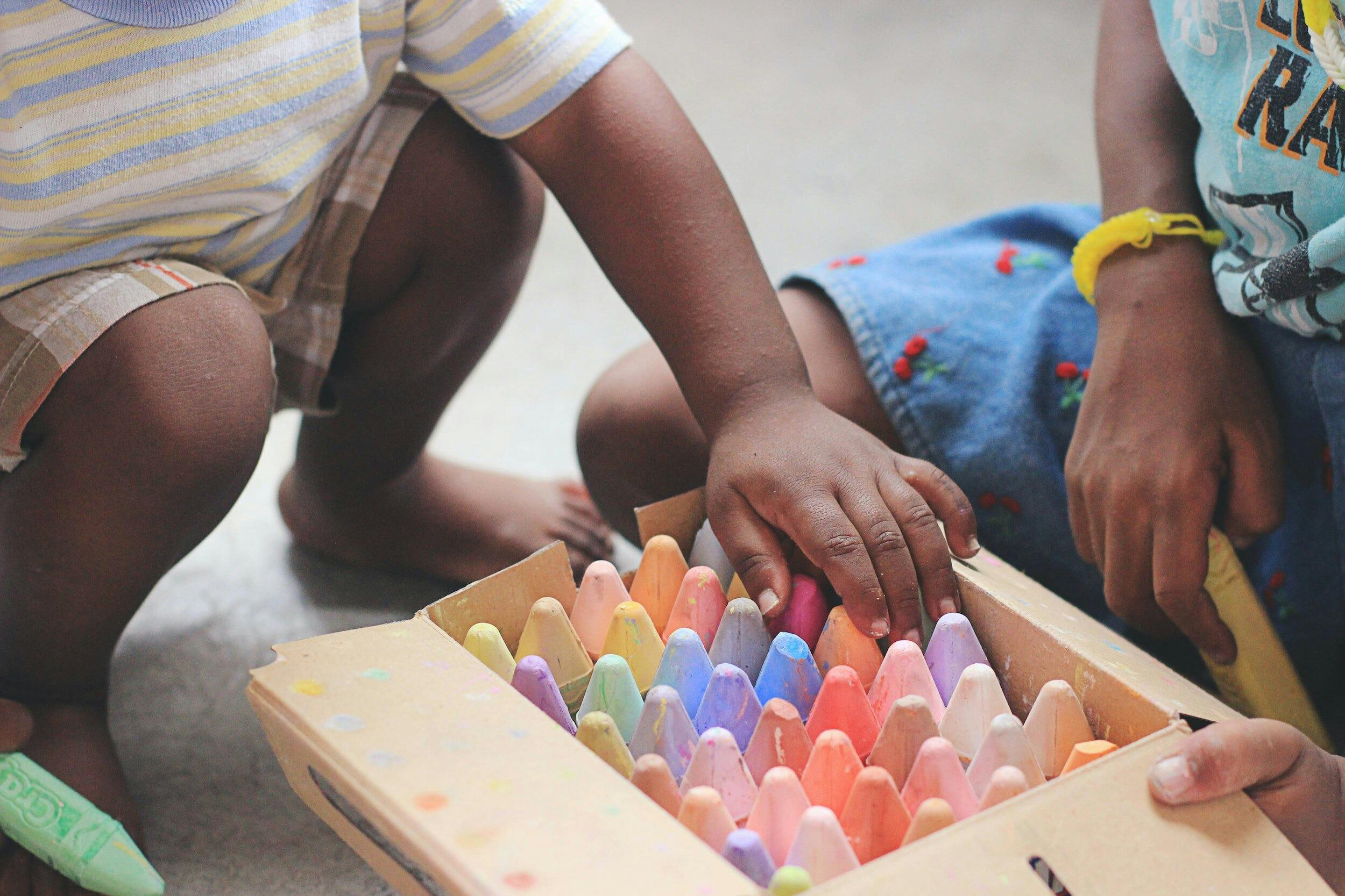 Children reaching for colorful sidewalk chalk in a box