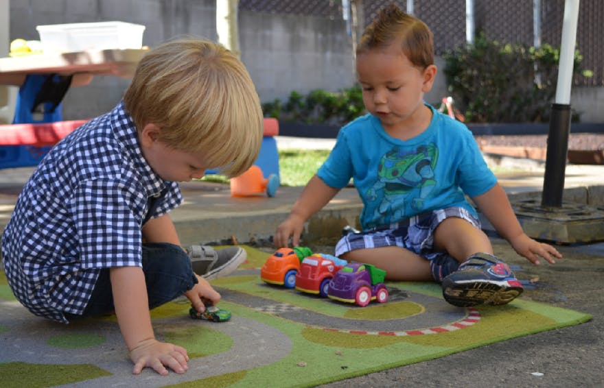 Two children playing with toy cars on a mat