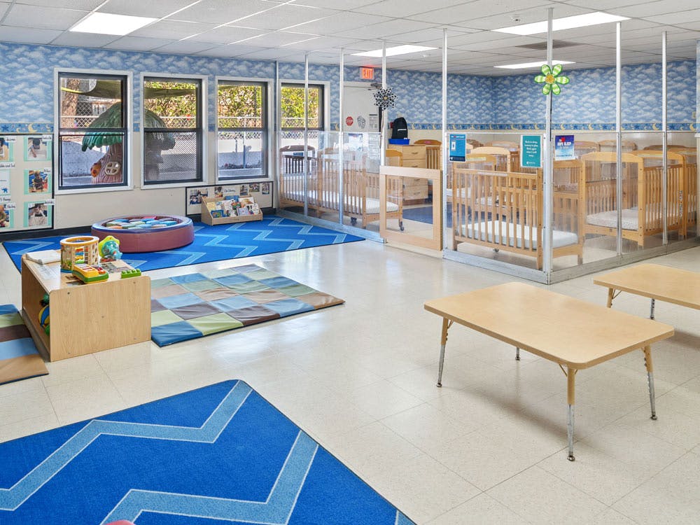Empty infant classroom with cribs, playmats, and small tables