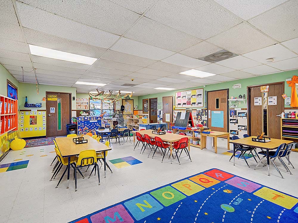 Empty classroom with small tables and chairs, colorful rugs, and decorations