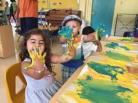 Two children with painted hands making art