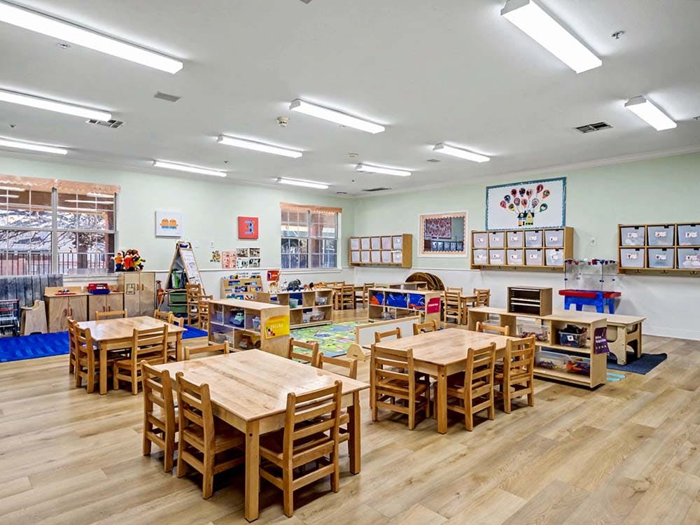 Empty classroom with small wooden tables and chairs, shelves with bins
