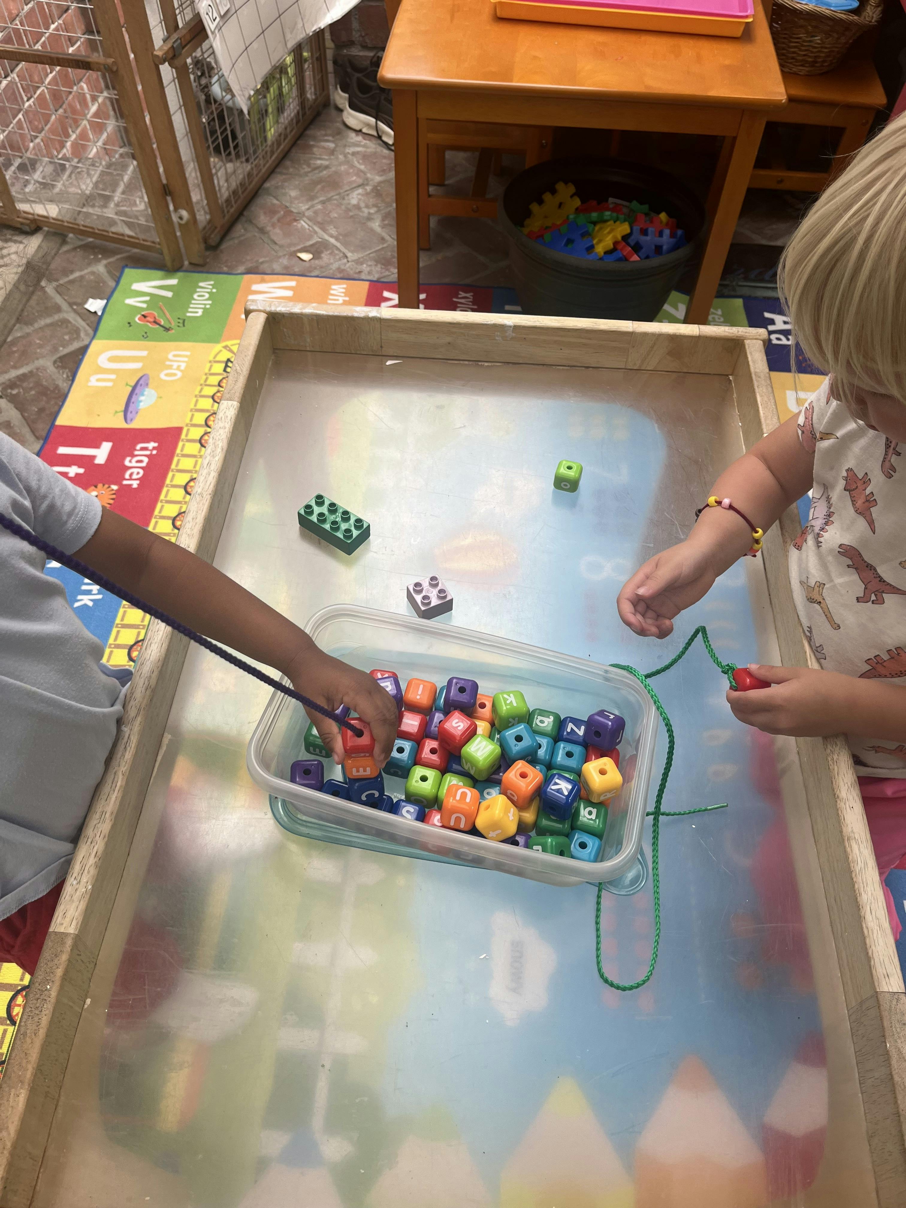 Children using string to fish for alphabet cubes in a plastic container