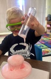 Child in safety goggles pouring liquid into a pink science experiment