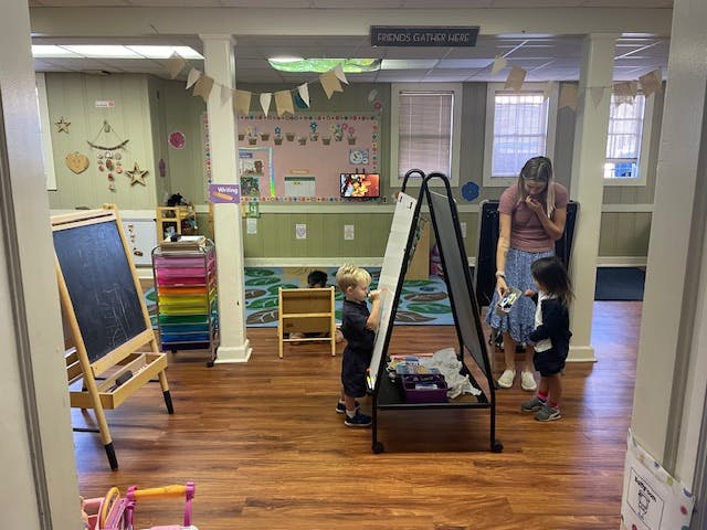 Adult and two children drawing on easels in a classroom