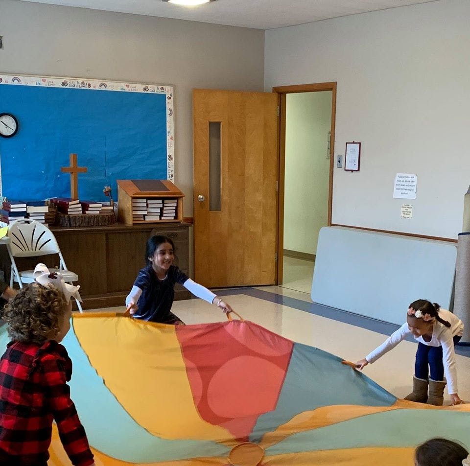 Three children playing with a colorful parachute in a classroom