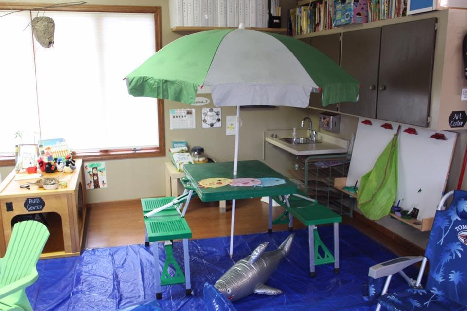 Indoor play area with green and white umbrella over a green table and chairs
