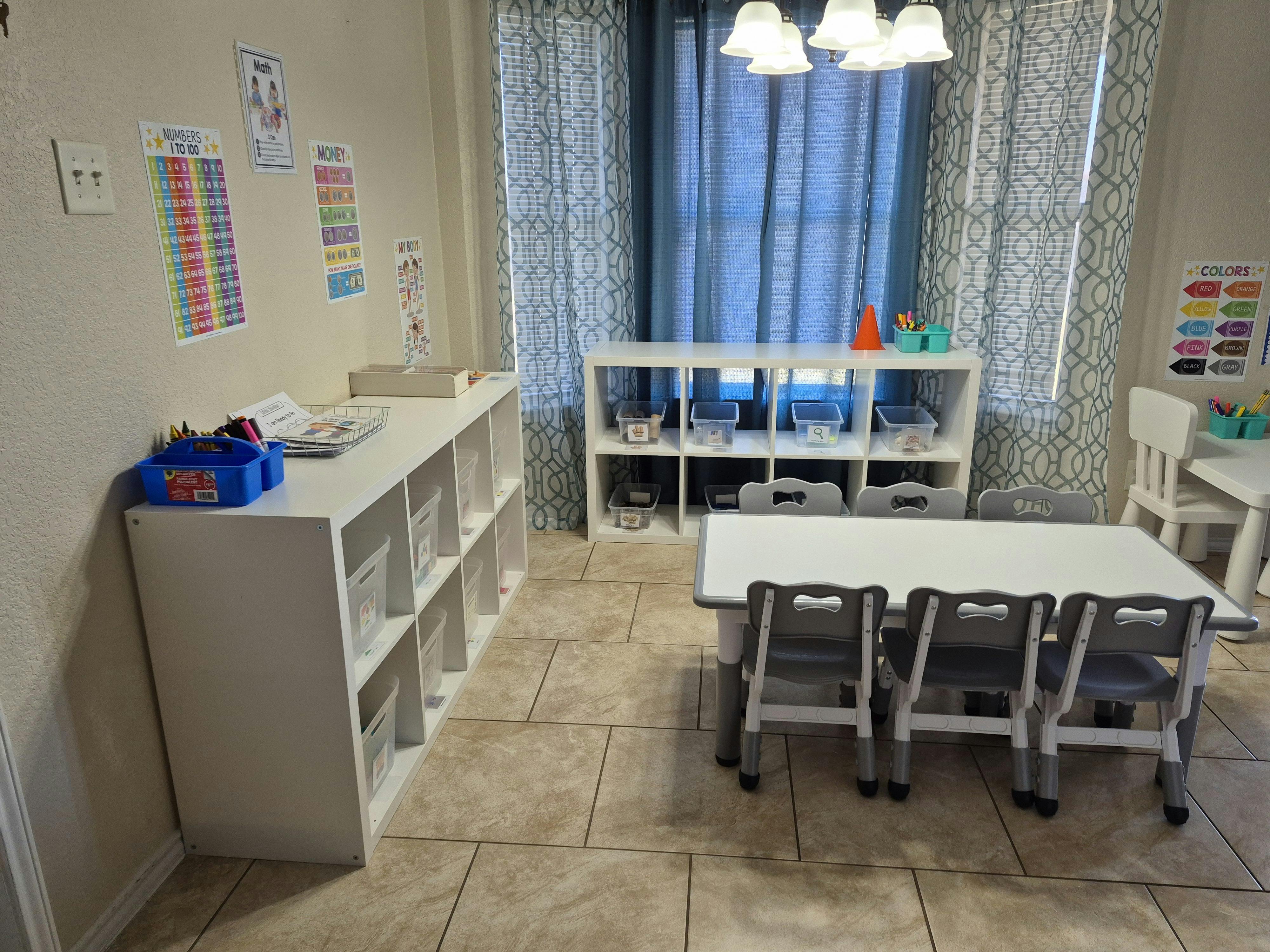 Classroom with small tables and chairs, shelves with storage bins, and educational posters