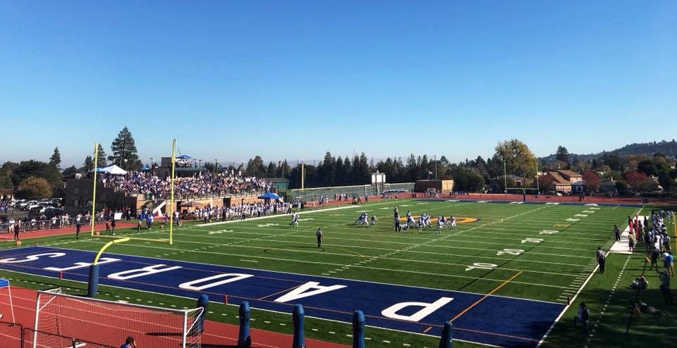 Football players on a field with bleachers full of spectators