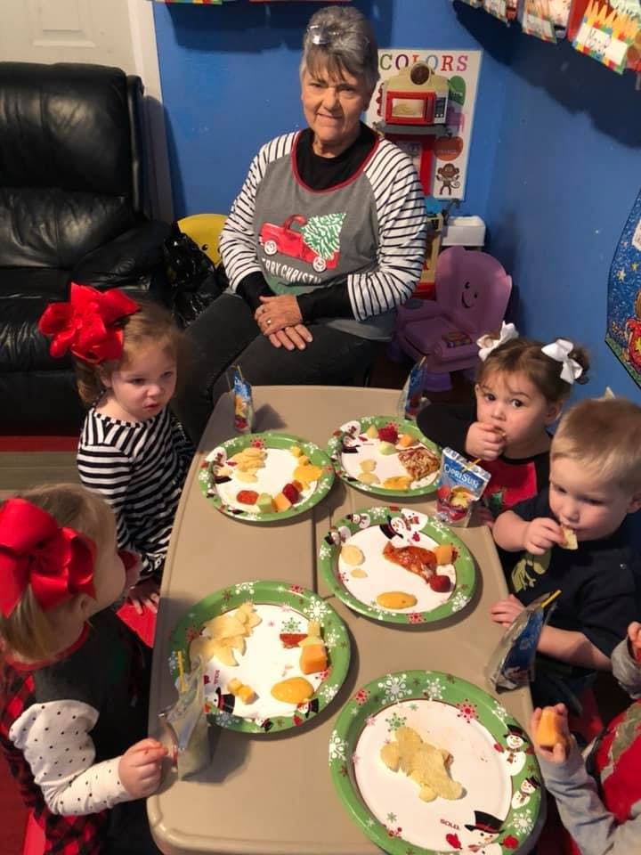 Adult person sitting at a table with several children eating snacks
