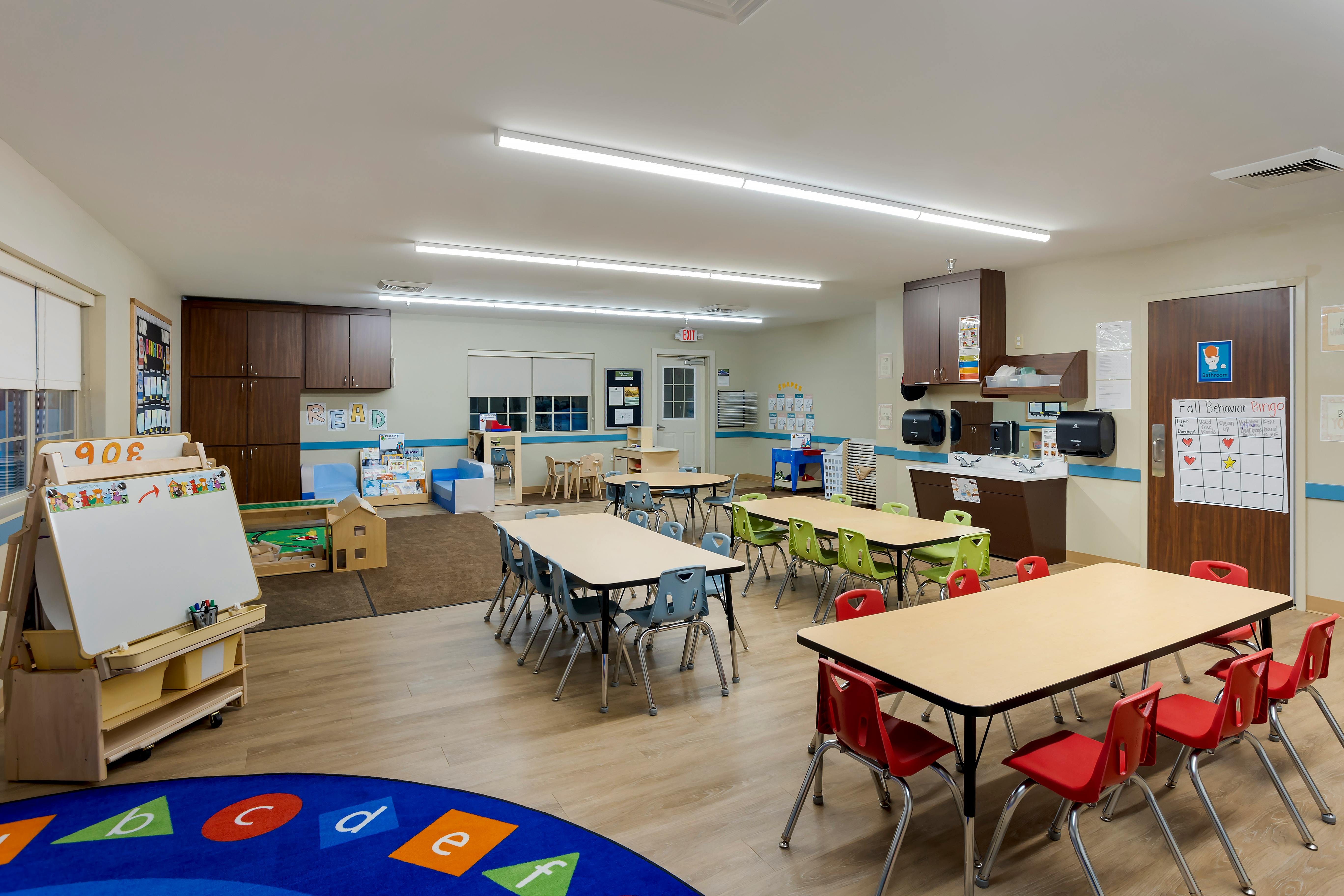 Classroom with child-sized tables and chairs, a sink counter, and an easel whiteboard