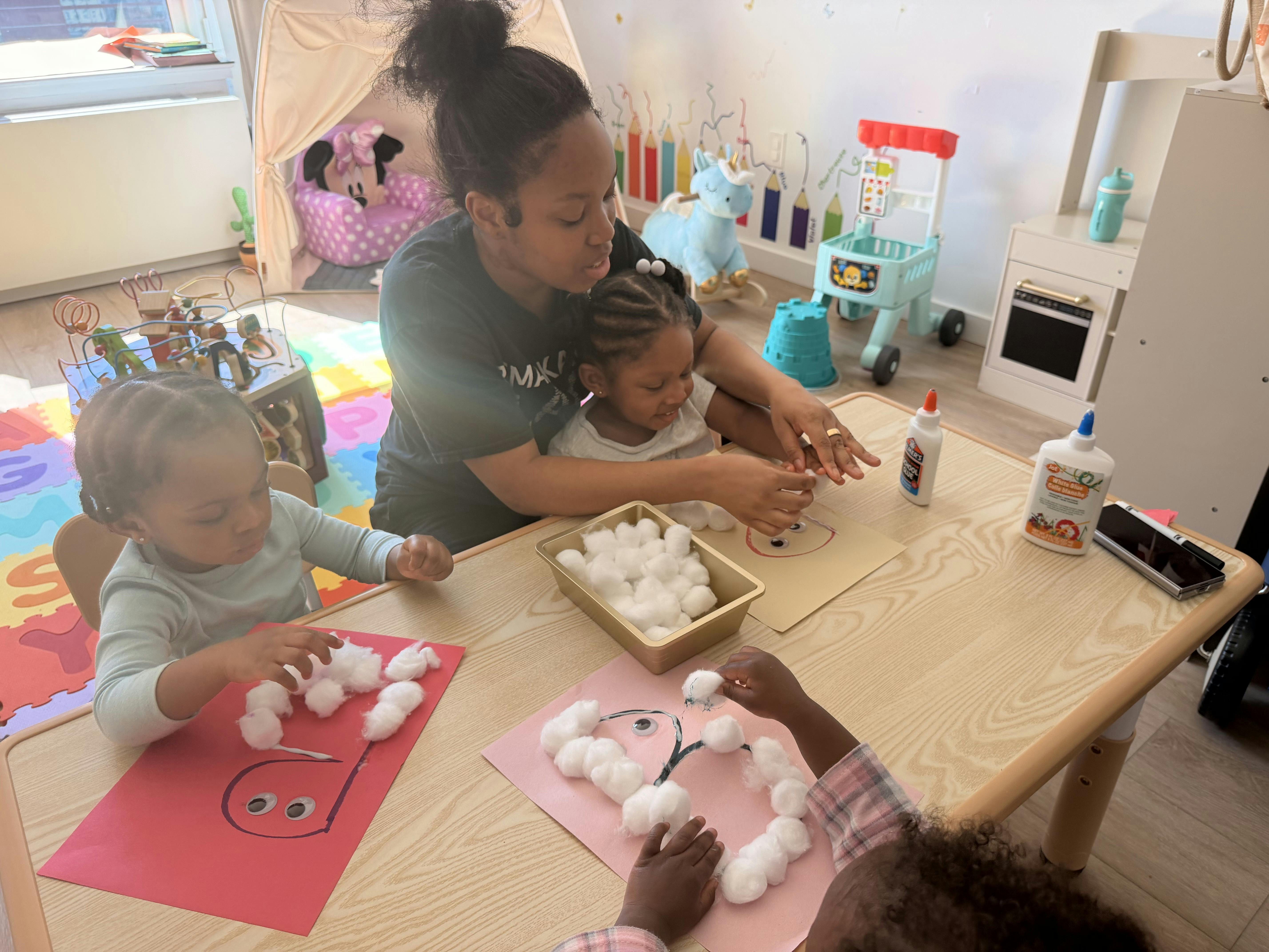 A person helping children with a cotton ball craft project at a table