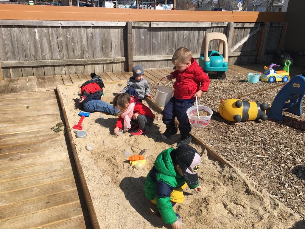 Multiple children playing in a sandbox with toys