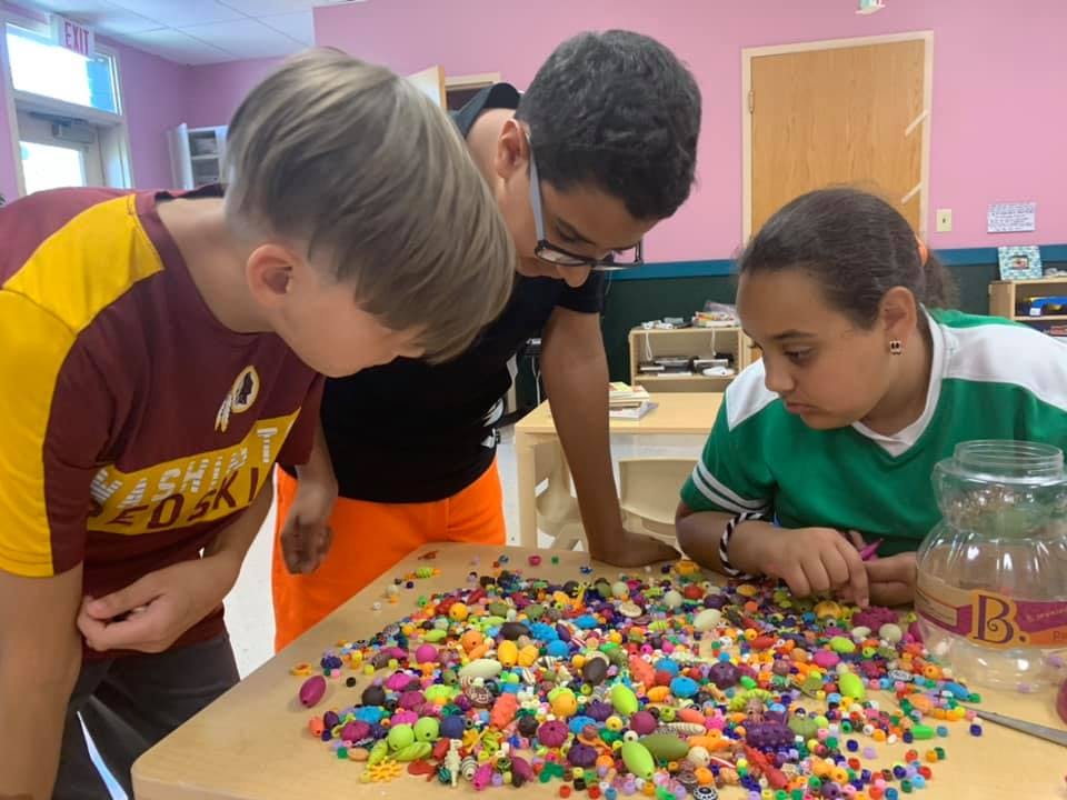 Three children looking at a pile of colorful beads on a table