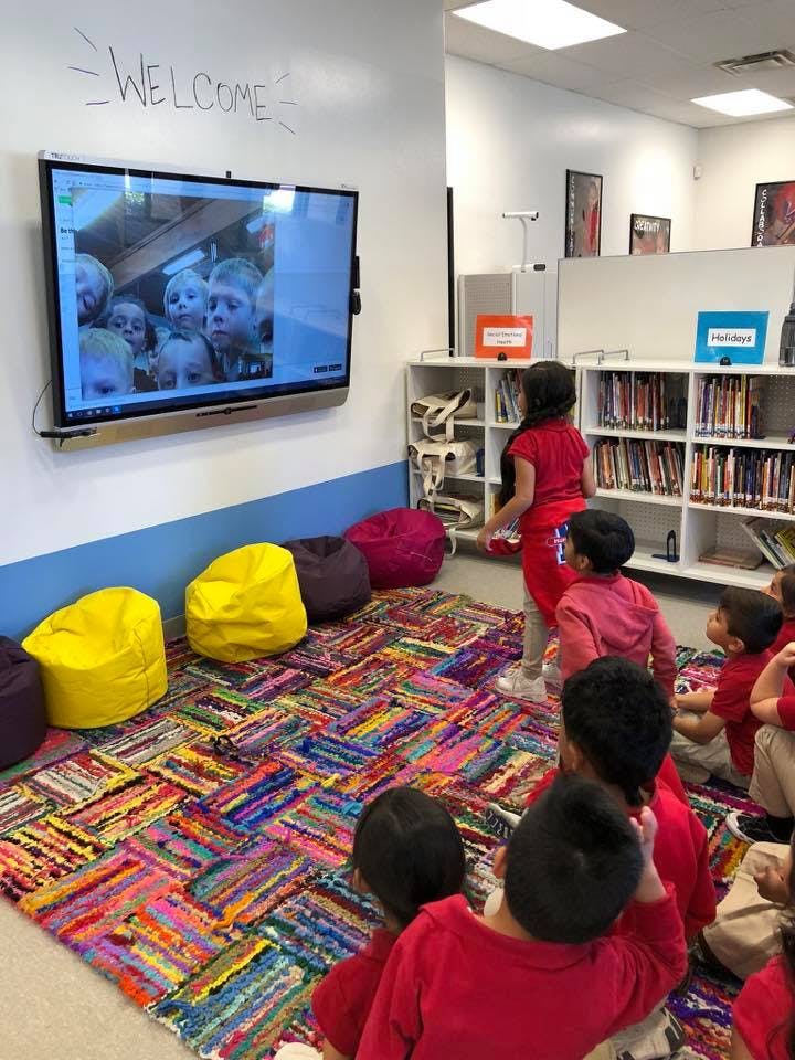 Children watching a screen in a classroom with a "WELCOME" sign