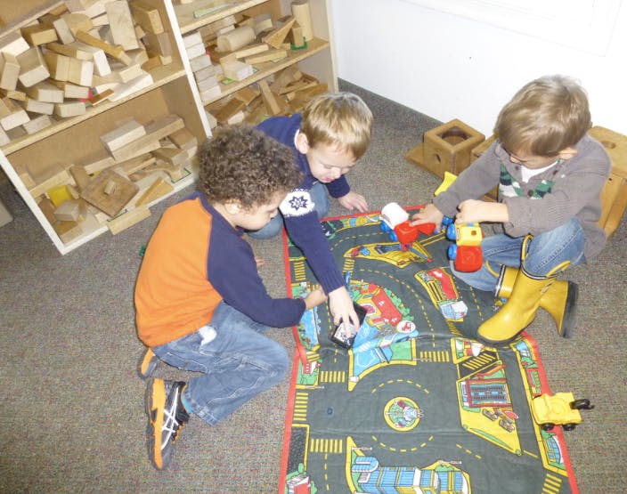 Three children playing with toy cars on a road mat