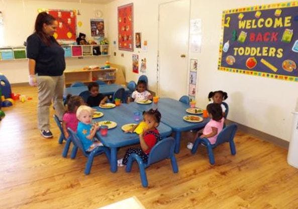 Adult standing near children seated at tables in a classroom