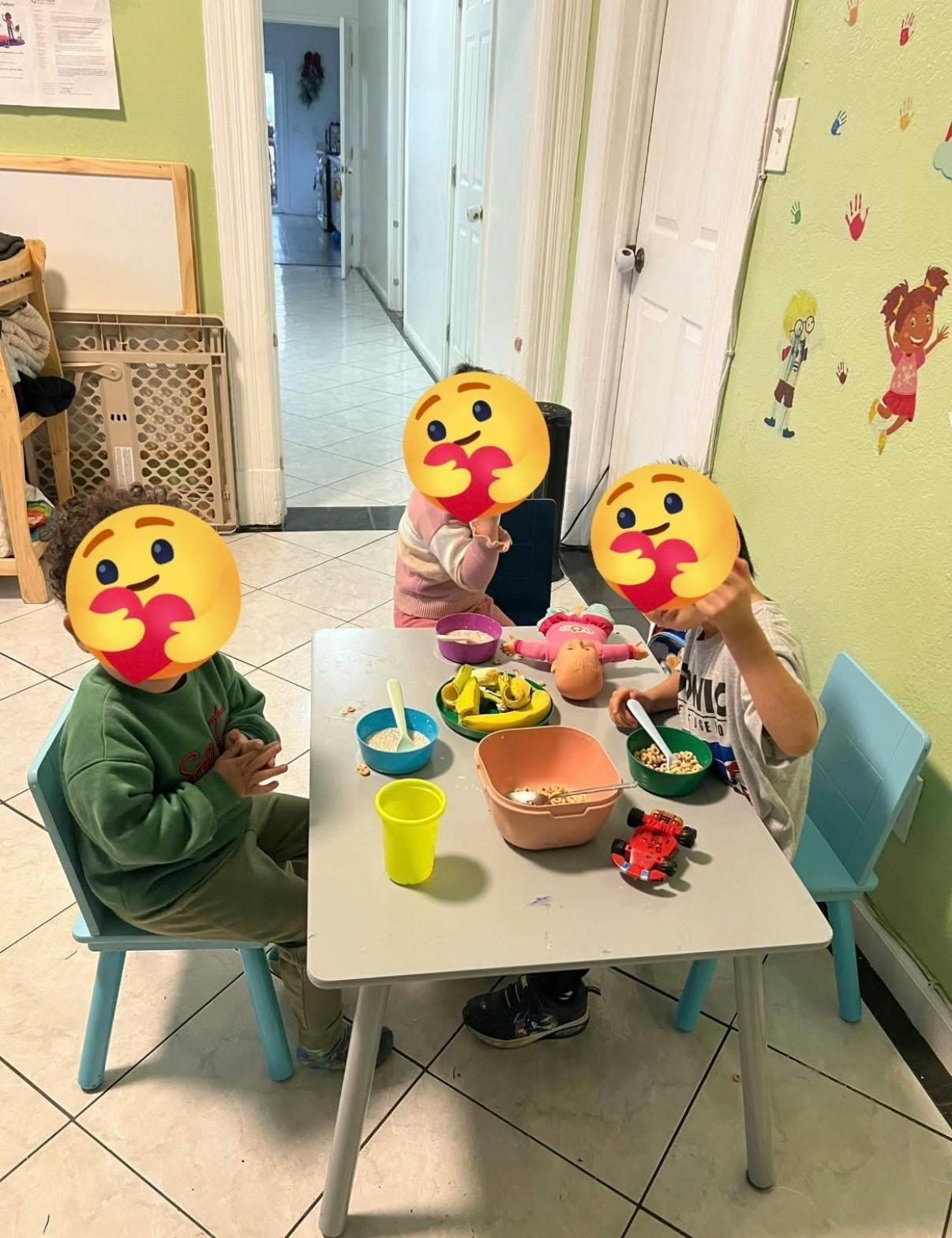 Three children sitting at a table with bowls of food and a toy car